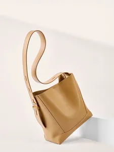 Minimalistische Beuteltasche aus Leder in Karamell mit breitem Gurt auf weißem Podest