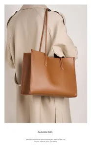 Bolso tote de cuero marrón colgado del hombro con gabardina beige sobre fondo blanco liso