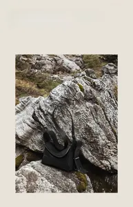 Détail d'un sac bandoulière en cuir grainé noir posé sur un décor de roche naturelle