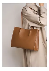Primer plano de un bolso tote de cuero marrón grande llevado por una modelo con gabardina