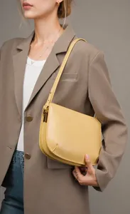 Close-up of a minimalist yellow leather underarm bag with gold buckle on a model
