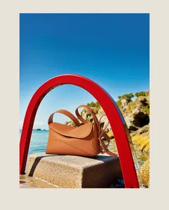 Détail d'un sac bandoulière en cuir caramel avec rabat ondulé sur socle face à la mer