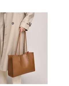 Primer plano de bolso tote de cuero marrón con costuras finas y pequeño logo dorado