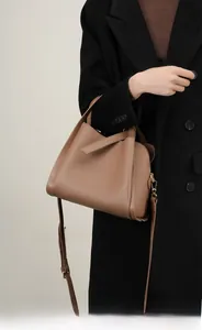 Borsa a secchiello in pelle martellata marrone portata a tracolla su un cappotto nero lungo
