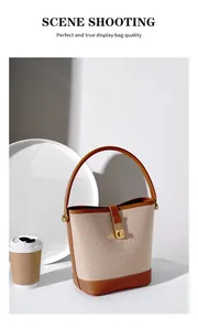 Detail of elegant beige canvas bucket bag with brown leather trim and gold metal lock clasp