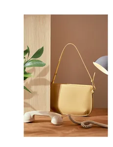 Detail of a creamy yellow leather underarm bag with gold metal buckle on a warm backdrop