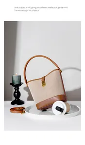 Detail of beige canvas bucket bag with brown leather trim and metallic buckle closure
