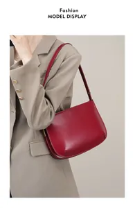 Detail of burgundy leather shoulder bag with gold hardware worn with a khaki blazer