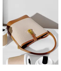 Detail view of woven bucket bag with cream fabric, brown leather trim and golden lock