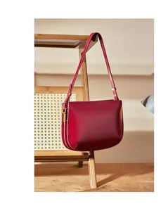 Detailed macro view of dark red leather texture and shiny gold hardware on the shoulder bag