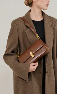 Close-up of brown leather underarm bag with gold turn-lock buckle on a blazer