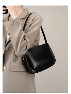 Detail of black glossy leather shoulder bag with gold hardware on a khaki blazer