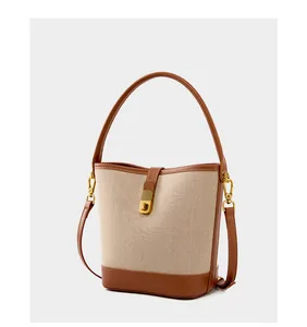 Detail of woven canvas bucket bag featuring premium brown leather trim and gold metal clasp