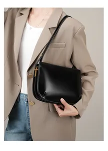 Detail of minimalist black leather shoulder bag with gold T-shaped metal hardware buckle