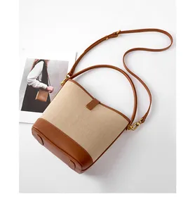 Detail of beige canvas and brown leather bucket bag with gold hardware and strap