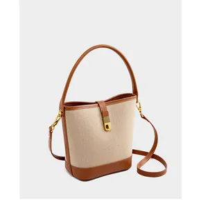 Detail of canvas bucket bag with brown leather trim and golden metal swivel clasp
