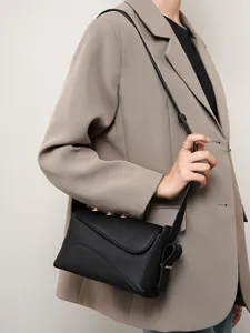 Sac bandoulière en cuir grainé noir porté par un mannequin en veste de costume beige