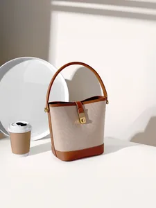 Chic beige canvas bucket bag with brown leather trim and gold metal clasp on white surface