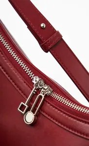 Detail view of burgundy leather shoulder bag with dual metal zippers and unique pullers