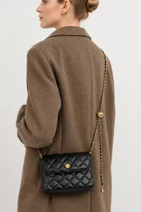 Detail of black quilted leather crossbody bag with gold floral clasp on a coat