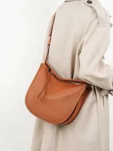 Minimalist leather tote bag in caramel brown worn by model in a stylish trench coat