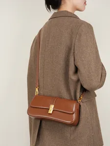 Brown leather baguette shoulder bag with gold buckle worn with a stylish blazer