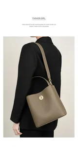 Borsa a secchiello in pelle taupe con chiusura a scatto su modella in abito nero