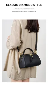 Detailed shot of a black pebbled leather Boston bag with gold hardware on a beige shirt