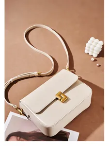 Detail of beige leather crossbody bag featuring a matte gold square clasp and strap