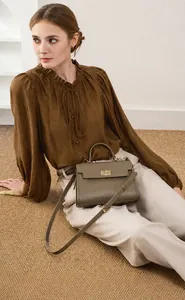 Détail d'un sac bandoulière en cuir marron avec boucle dorée sur un mannequin assis