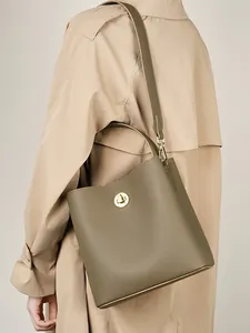 Borsa a secchiello in pelle verde oliva con chiusura dorata indossata con trench