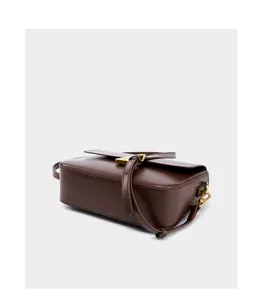 Detailed side view of dark brown leather handbag with gold metal clasp and adjustable strap