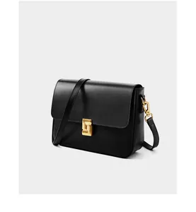 Close-up of black leather crossbody bag featuring a golden geometric clasp and fine texture