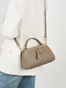Taupe pebbled leather Boston bag with gold hardware worn by model on white background