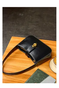 Détail d'un sac sous les bras en cuir noir avec boucle dorée sur table en bois
