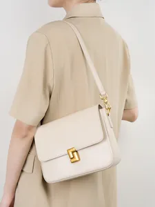 Minimalist cream leather square crossbody bag with gold buckle on female model shoulder