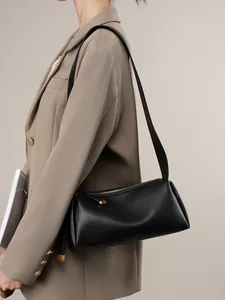 Sac sous le bras en cuir noir minimaliste avec détails dorés porté par un mannequin