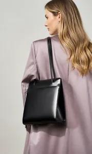 Close-up of minimalist black leather tote bag with long shoulder straps on a blazer model