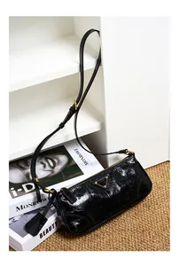 Detail of glossy oil wax leather shoulder bag featuring a triangular metal logo plaque