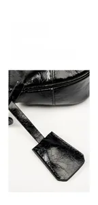 Detailed close-up of glossy black oil wax leather shoulder bag with decorative hangtag