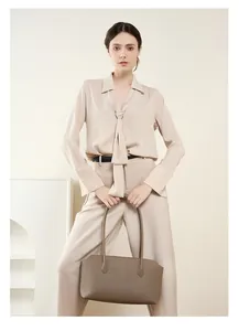 Donna elegante con borsa tote in pelle marrone e camicia di seta in un ambiente moderno