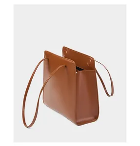 Détail d'un sac cabas minimaliste en cuir marron montrant la texture lisse et les anses