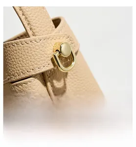 Macro detail of beige pebble leather texture and gold D-ring hardware on handbag