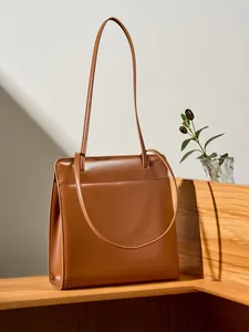 Sac fourre-tout minimaliste en cuir marron avec fines bandoulières sur support en bois