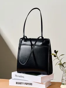 Grand sac cabas minimaliste en cuir noir brillant posé sur des livres de décoration