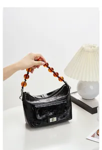Détail du sac plissé en cuir verni noir avec poignée en perles d'ambre et fermoir rotatif