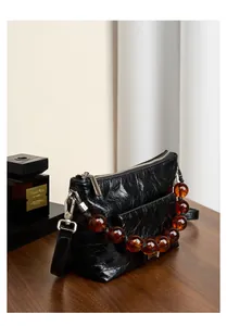 Détail du sac bandoulière en cuir ciré noir avec une chaîne en perles d'ambre décoratives