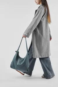 Detailed view of large dark teal leather tote bag worn with grey autumn overcoat