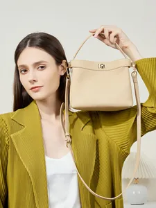 Elegant beige pebbled leather bucket bag with gold clasp shown with a stylish suit