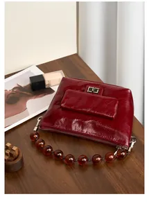 Détail d'un sac en cuir bordeaux avec anse à perles sur une surface en bois
